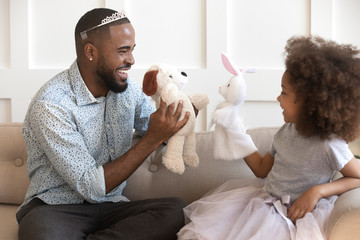 Happy african dad wearing crown holding toys playing with daughter