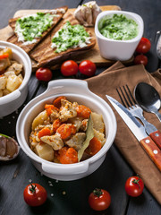 Close-up baked chicken with potatoes and carrots, cheese sandwiches and cherry tomatoes on a dark wooden background.