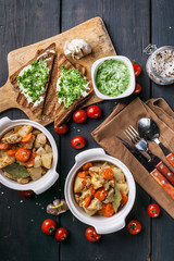 Baked chicken with potatoes and carrots, cheese sandwiches and cherry tomatoes on a dark wooden background. Top view