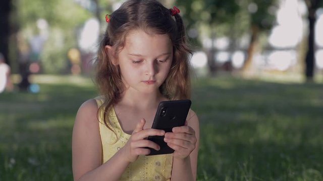 Girl in the park communicates with friends in social networks using a smartphone. Smiling teenager in chat using mobile phone, typing message, view photos or other interesting content on her gadget.