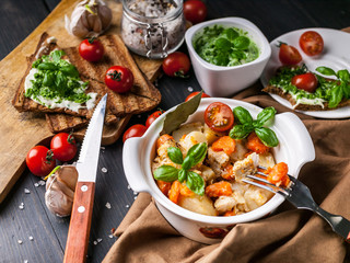 Close-up potatoes with chicken and vegetables, sandwiches with cheese and cherry tomatoes on a dark wooden background.