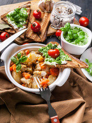 Close-up potatoes with chicken and vegetables, sandwiches with cheese and cherry tomatoes on a dark wooden background.