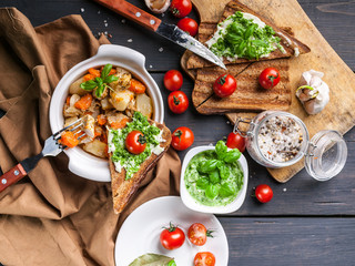 Top view potatoes with chicken and vegetables, sandwiches with cheese and cherry tomatoes on a dark wooden background.