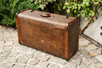 Old vintage retro grunge weathered suitcase on stone paved house backyard