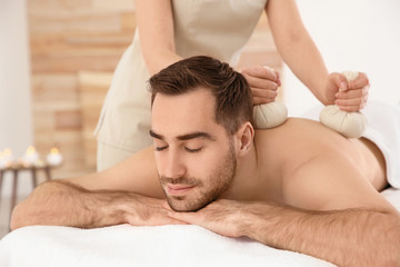 Fototapeta na wymiar Handsome man receiving herbal bag massage in spa salon