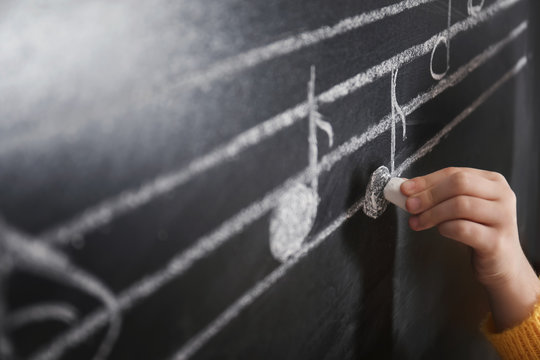 Child Writing Music Notes On Blackboard, Closeup