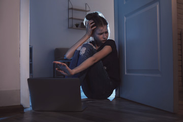 Frightened teenage girl with laptop on floor in dark room. Danger of internet