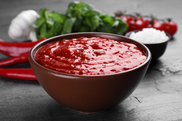 Bowl of spicy chili sauce on grey table, closeup