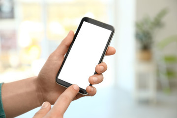Man holding smartphone with blank screen indoors, closeup of hands. Space for text