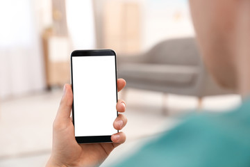 Man holding smartphone with blank screen indoors, closeup of hand. Space for text