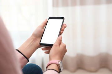 Woman holding smartphone with blank screen indoors, closeup of hands. Space for text