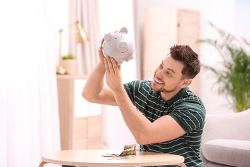 Man with piggy bank and money at home