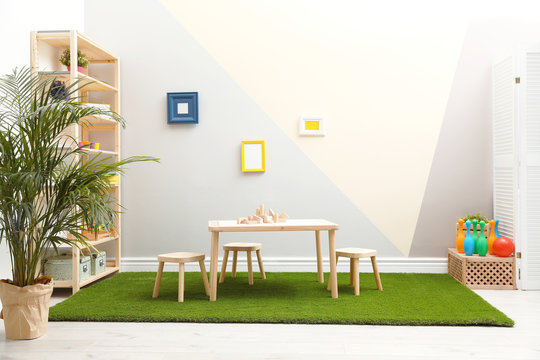 Stylish playroom interior with table, stools and green carpet