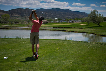 Young Male Golfer Hitting a Golf Ball Off of the Tee Box - Mountains in the background