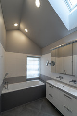 Bathroom interior in the attic. Bath, cabinet with sink and two water taps, mirror, window and sunroof.