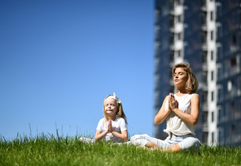 Mother and daughter together practicing yoga outside on a grass together urban city 