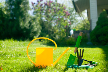 Close up of Gardening tools on the green grass lawn. Countryside view. Landscape. Still life. View of hoe, shovel, scoop, gloves, rubber shoes and watering can.. - 271867961