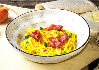 Pumpkin noodles with bacon, green leaves and parmesan. Pasta Carbonara on white plate with parmesan on white fabric background.