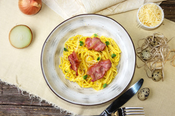 Pumpkin noodles with bacon, green leaves and parmesan. Pasta Carbonara on white plate with parmesan on white fabric background.