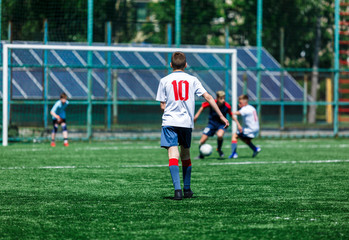Boys in white and blue sportswear plays  football on field, dribbles ball. Young soccer players with ball on green grass. Training, football, active lifestyle for kids concept 