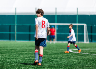 Boys in white  sportswear plays  football on field, dribbles ball. Young soccer players with ball on green grass. Training, football, active lifestyle for kids concept 