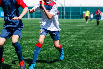 Boys in white and blue sportswear plays  football on field, dribbles ball. Young soccer players with ball on green grass. Training, football, active lifestyle for kids concept 