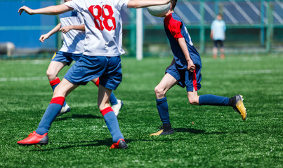 Boys in white and blue sportswear plays  football on field, dribbles ball. Young soccer players with ball on green grass. Training, football, active lifestyle for kids concept 