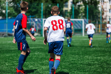 Boys in white and blue sportswear plays  football on field, dribbles ball. Young soccer players with ball on green grass. Training, football, active lifestyle for kids concept 