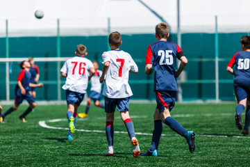 Boys in white and blue sportswear plays  football on field, dribbles ball. Young soccer players with ball on green grass. Training, football, active lifestyle for kids concept 