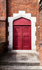 Exterior rich red arched doorway in a brick wall, framed in stone. No handles on doors.