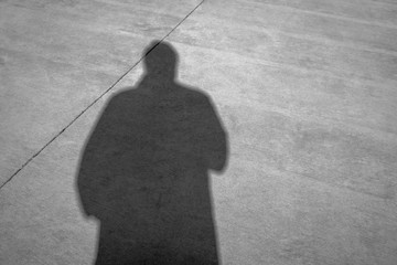 Large and looming shadow of man in overcoat against cold concrete. Copy space, concept, background, black and white