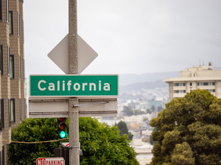 Fototapeta premium California street sign hanging in San Francisco in front of city and green light and foggy sky
