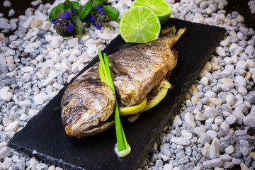 Delicious grilled dorado fish with lime and chives on a black stone plate.