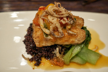 A plate of fish cutlet servied on squid ink risotto and fried calamaries place on top.