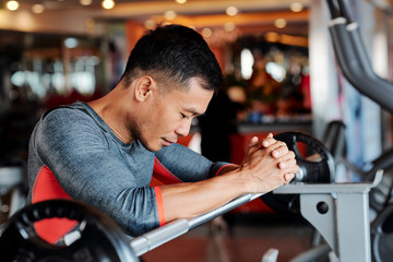 Exhausted sportsman leaning on gym equipment when resting between sets