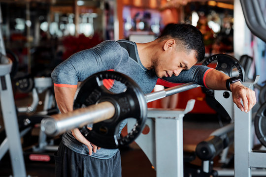 Tired Young Vietnamese Man Standing At Workout Bench And Leaning On Barbell After Doing Exercise