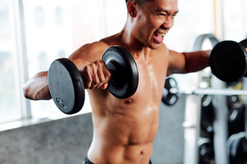Shirtless fit man shouting when doing side lateral rises with heavy dumbbells