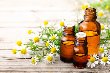 Chamomilla essential oil in the amber bottle, with fresh flowers, on the old wooden board