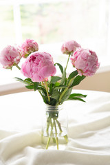 Vertical close up of a transparent vase of pink peonies flower bouquet on a white table