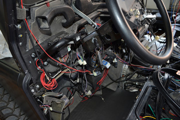 A lot of ravel multicolored wires from the car wiring lies in the cabin of dismantled car with connectors and plugs, a view through the window inside the battered car. Auto service industry