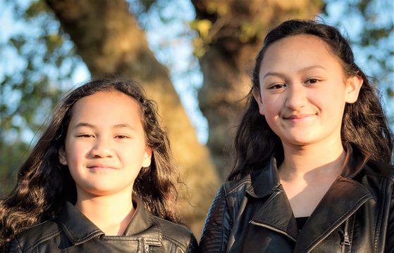Portrait of two young Maori sisters taken outdoors in a park.