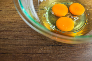 Three raw chicken egg yolk and white in glass bowl on top of wooden table top.	