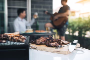 Close up grilled meats and various food on the grill and celebrations of friends who are playing guitar and sing together in their home. - obrazy, fototapety, plakaty