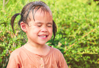 Cute asian little child girl having fun to play with water spraying hose in summer garden.