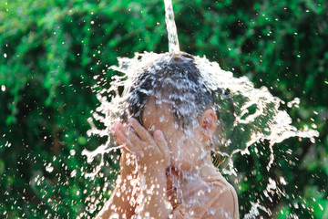 Cute asian little child girl having fun to play with water spraying hose in summer garden.