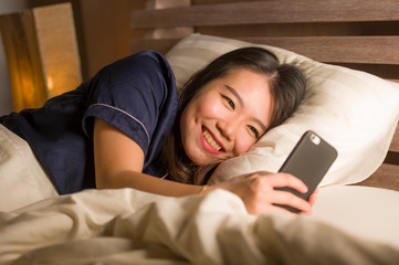 young beautiful and happy Asian Japanese woman in pajamas using mobile phone social media texting with her boyfriend or enjoying online dating app smiling cheerful
