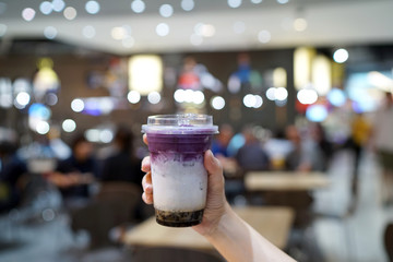 Purple sweet potato milk tea - Hand holding a glass of iced taro latte with boba or golden bubble on blurred background, Most Popular in Taiwan.