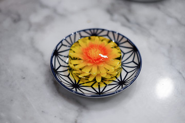 Yellow flowers in jelly on a white plate on a marble background. Pudding with colored flowers. Jelly cake in the shape of a flower. selective focus