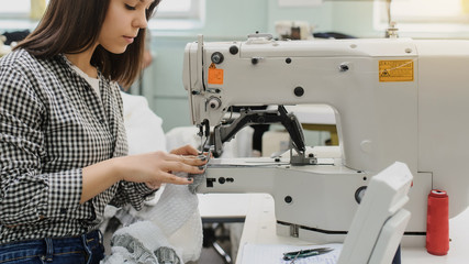 close up photo of a young woman sewing with sewing machine in a factory