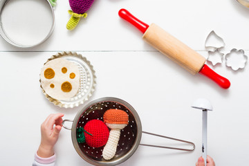 baby hands playing with craft knitted plush vegetables in children kitchen, directly above